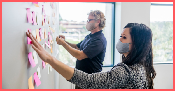 people wearing face masks putting sticky notes on a white board